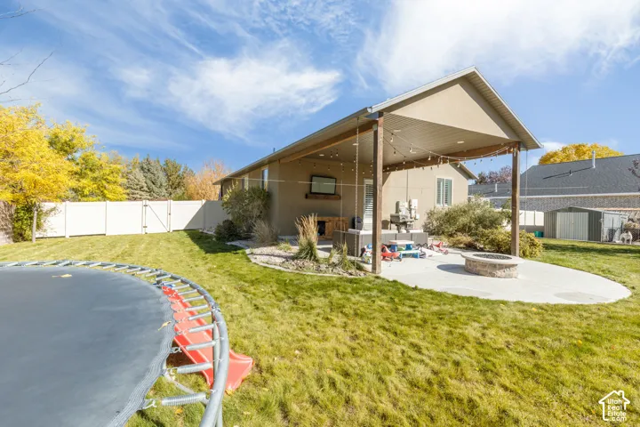 Rear patio featuring a covered area with recessed lighting, a circular stone-block fire pit, concrete hardscaping, and full vinyl privacy fencing
