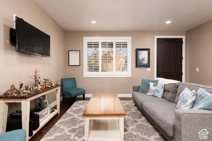 Living area featuring dark wood-finish flooring, recessed lighting, and a window with white louvered shutters