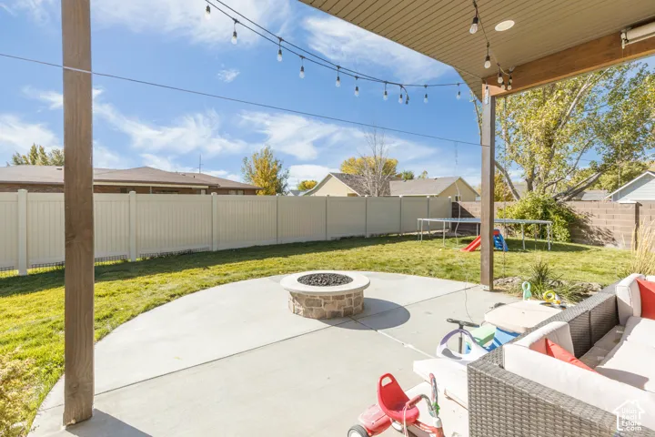 Covered patio featuring a concrete hardscape, stone fire pit, and string lighting, enclosed by a perimeter vinyl fence