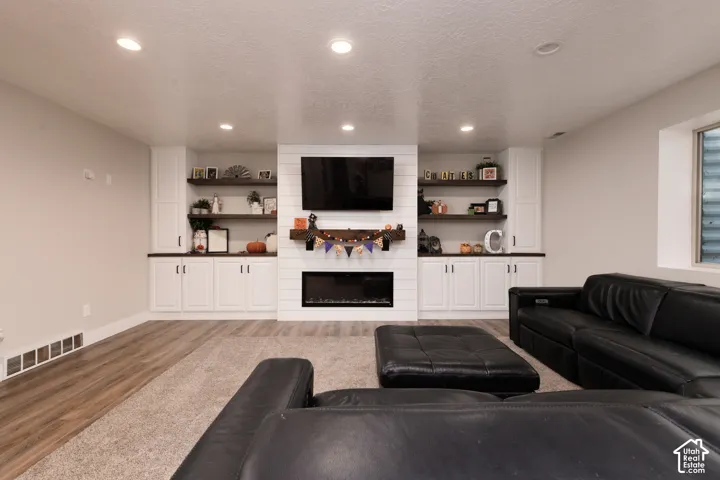 Built-in white cabinetry, horizontal shiplap fireplace surround, recessed lighting, wood-finish flooring, and natural wood floating shelves