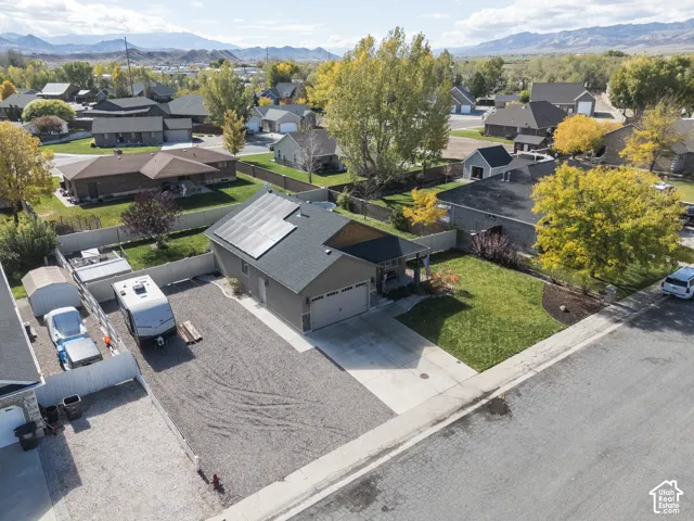 Single-level exterior featuring asphalt shingle roofing, integrated solar panels, concrete driveway, gravel side parking area, and enclosed yard space