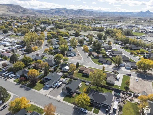 Aerial perspective of a suburban neighborhood featuring mature trees, paved streets, residential lots, and a distant mountain range backdrop