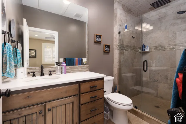 Bathroom featuring a wood-finish vanity with a light-toned countertop, large wall-mounted mirror, glass-enclosed shower with stone-style wall tile, and a decorative tile backsplash