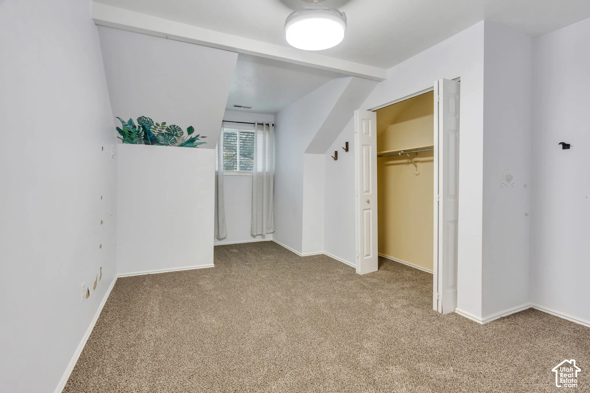 Room featuring carpeted flooring, vaulted ceiling, built-in closet with bifold doors, window with horizontal blinds, and ceiling-mounted lighting