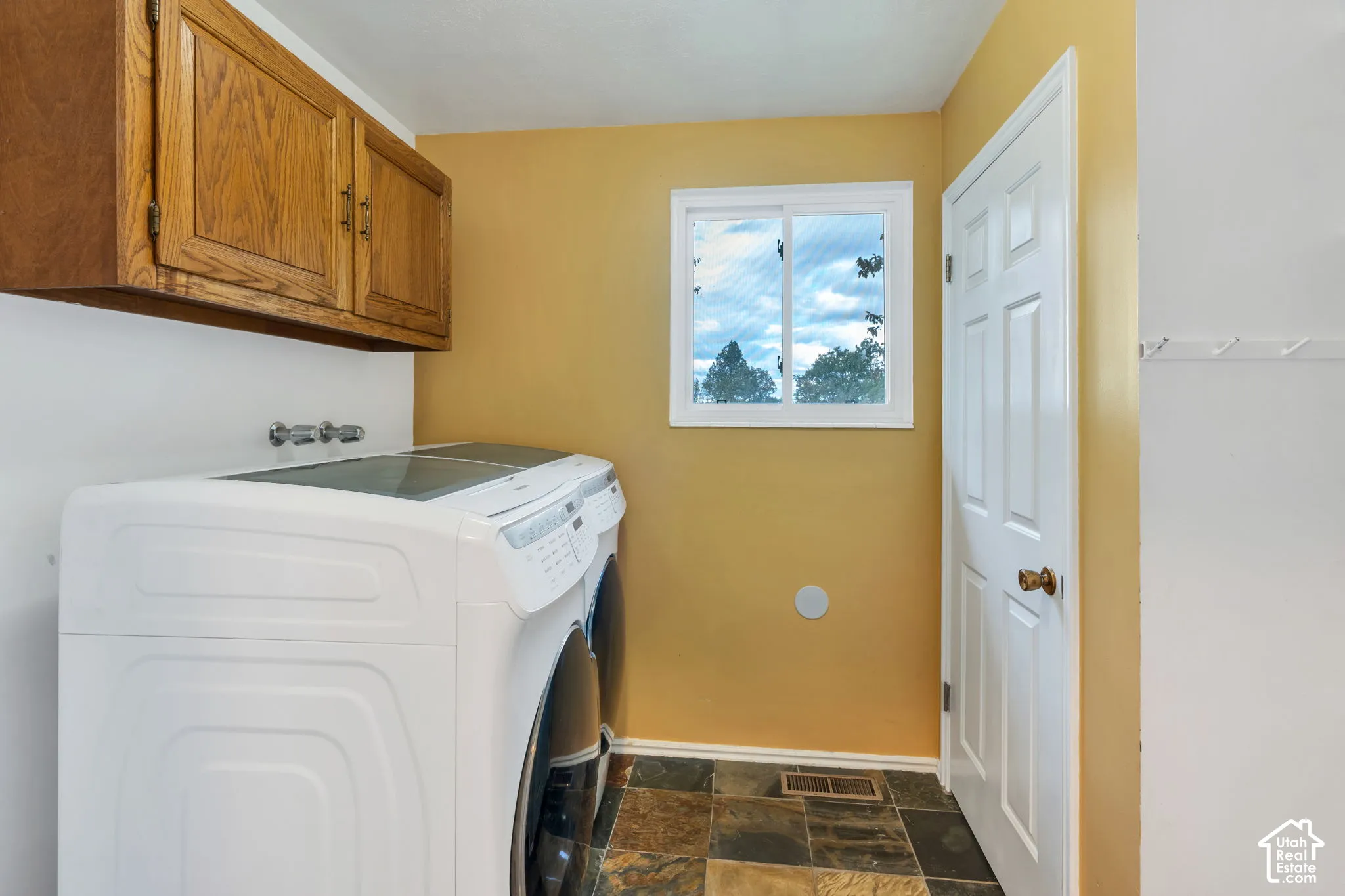 Laundry area featuring natural stone-tile flooring, wood-finish wall-mounted cabinetry, and a sliding window