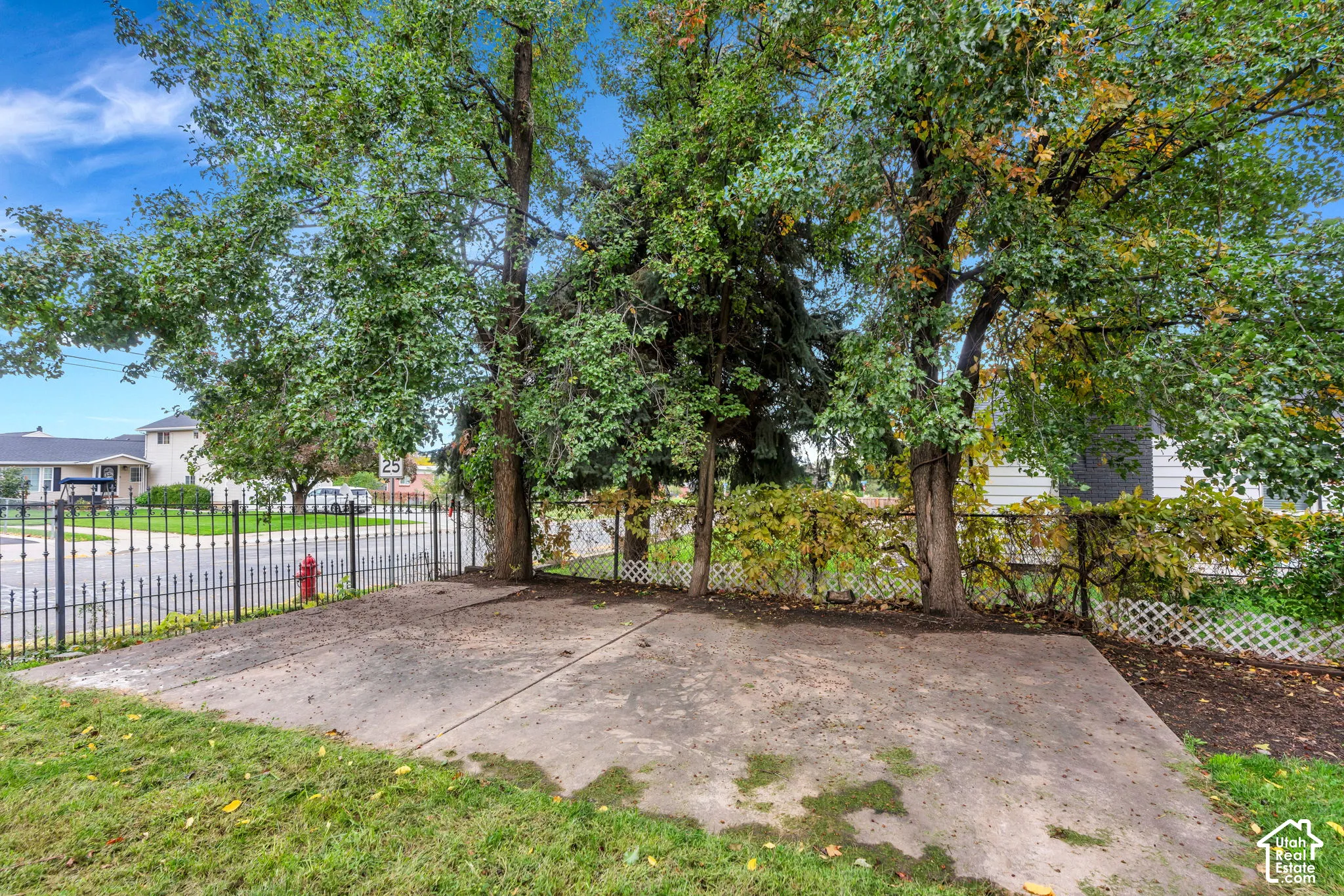Concrete patio slab bordered by mature trees, metal ornamental fencing, and lattice screen panels
