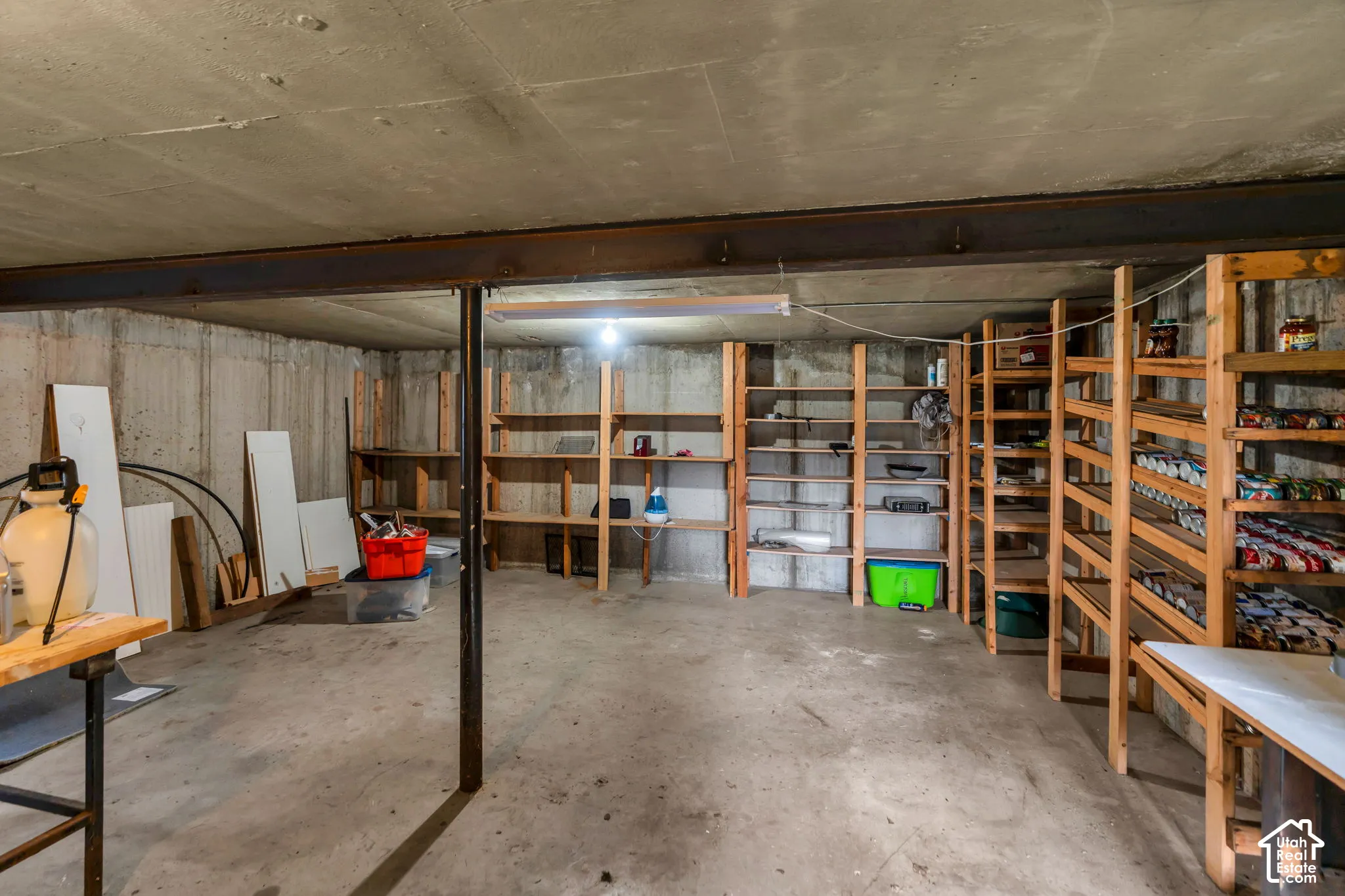Unfinished storage area featuring exposed concrete walls, concrete flooring, structural steel support beams, and built-in wood shelving units