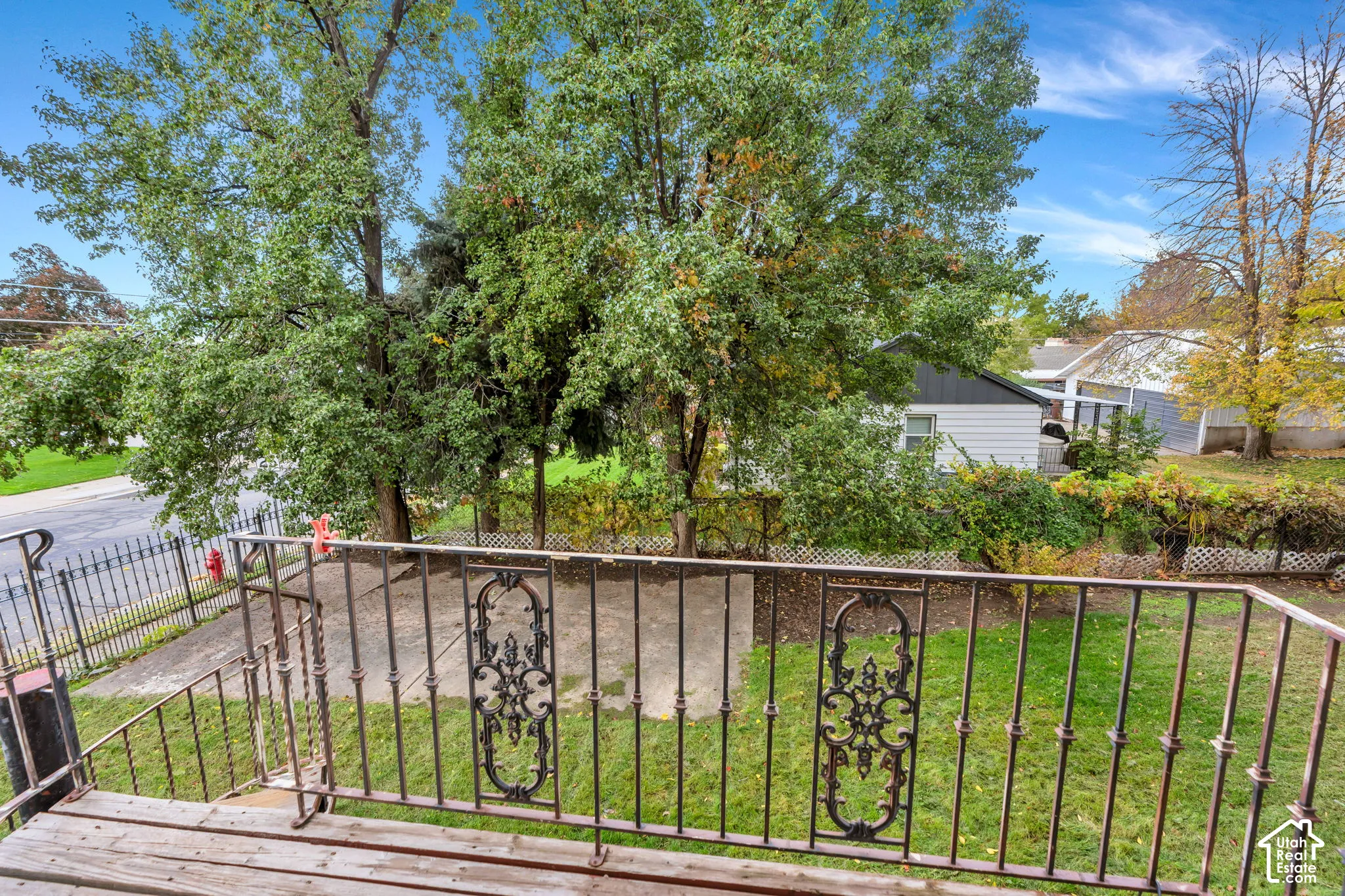 Elevated wooden deck featuring custom ornate metal railings, expansive lawn space, and mature trees