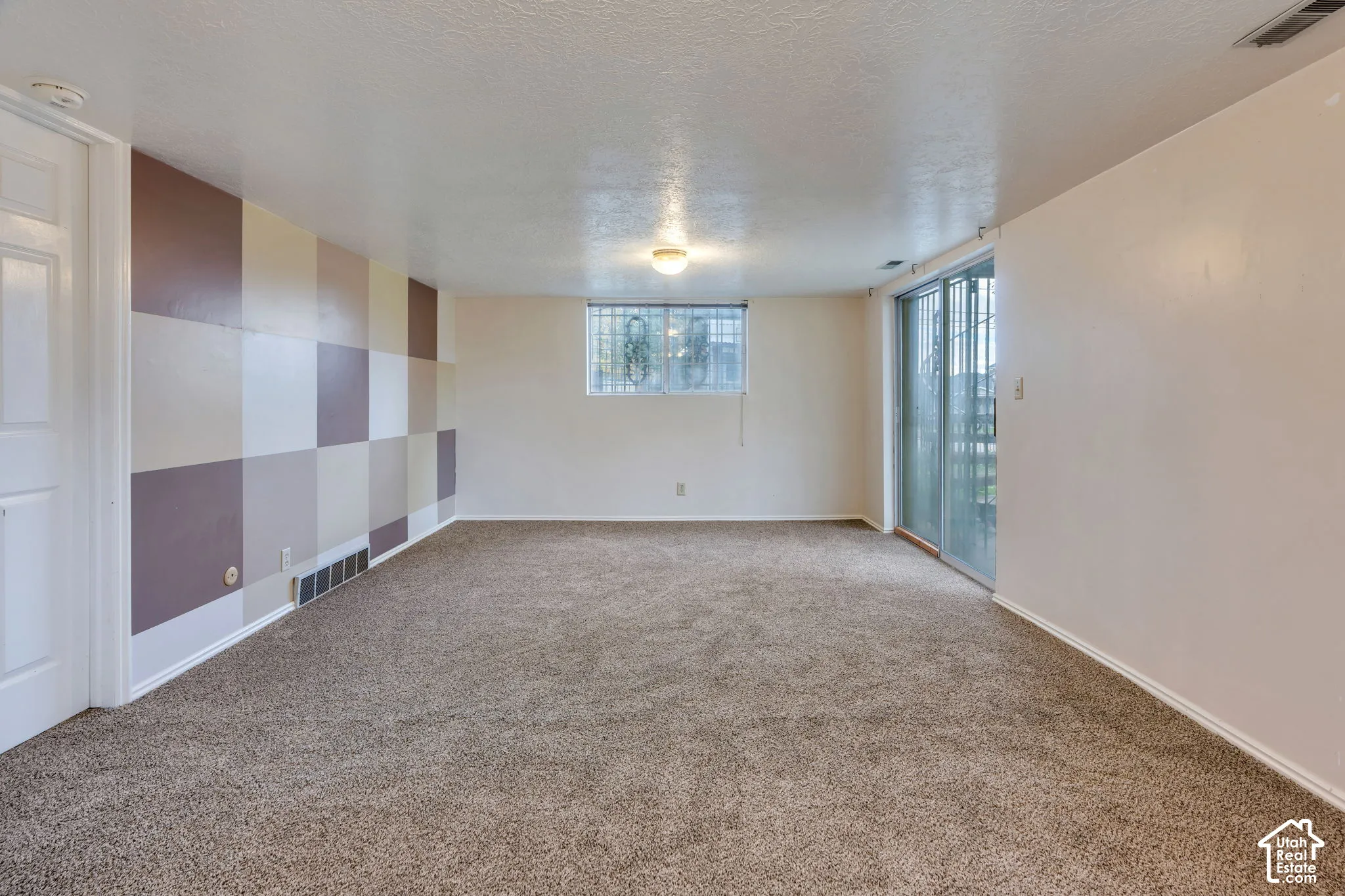 Neutral wall-to-wall carpeting, decorative multi-tone checkered wall paneling, sliding glass door, and large picture window