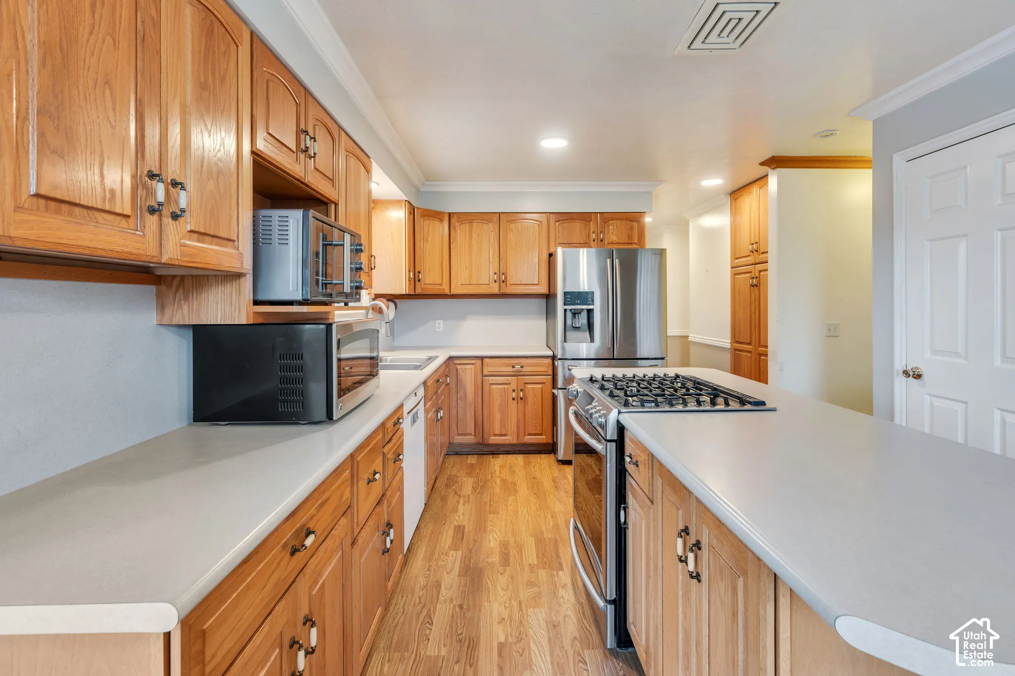 Kitchen featuring wood cabinetry, stainless steel appliances, a gas cooktop, solid-surface countertops, and wood-finish flooring