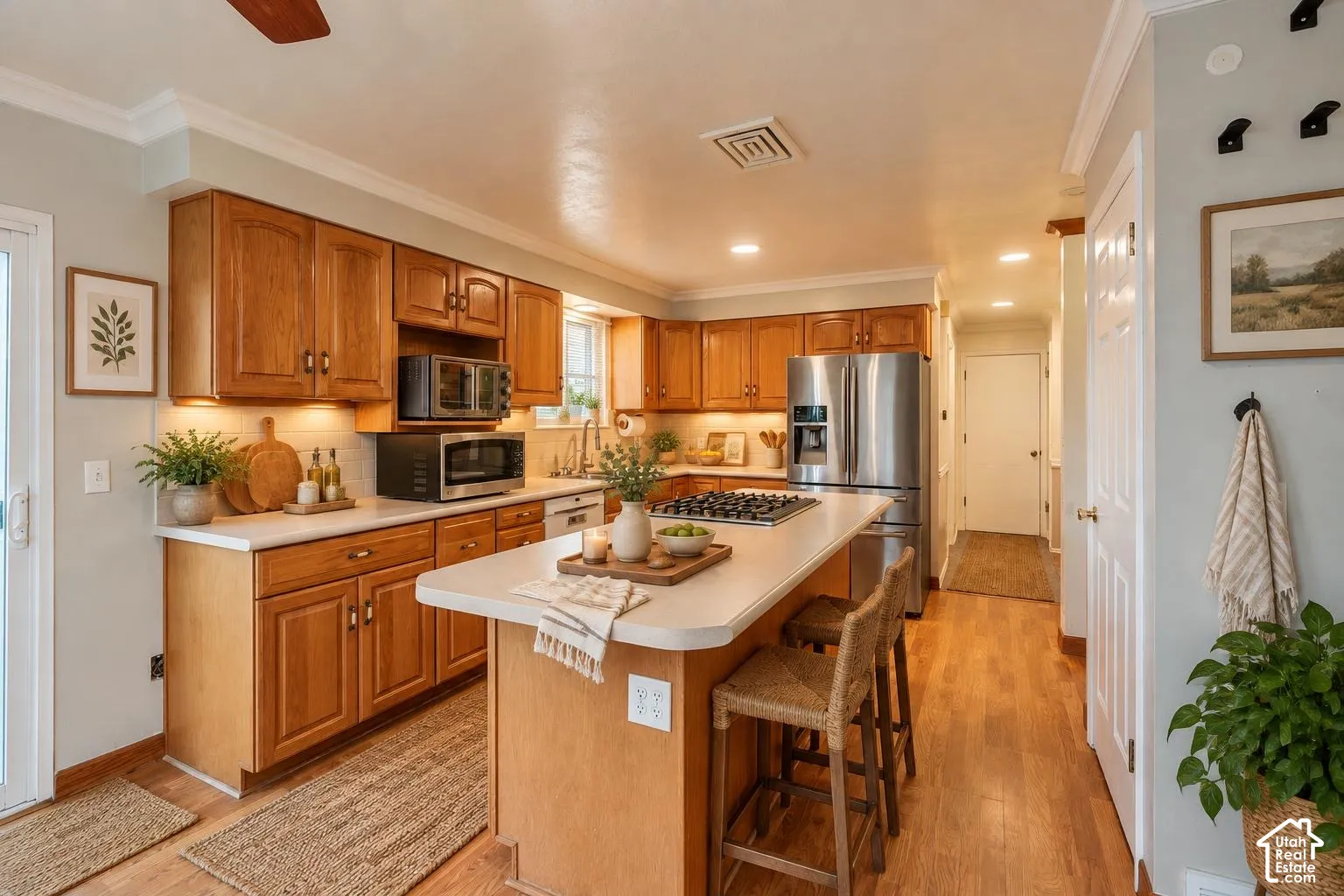 Kitchen featuring wood cabinetry, a central island with a cooktop, stone-finish countertops, stainless steel refrigerator, and wood-finish flooring