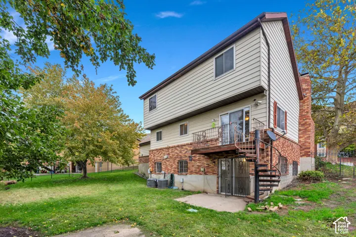 Two-story exterior featuring a brick and horizontal siding facade, a metal spiral staircase, a raised wooden deck, and an expansive lawn with mature trees