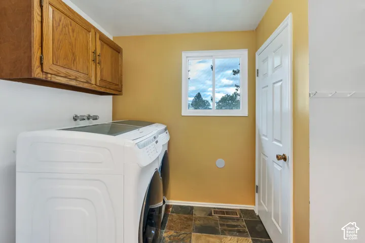Laundry area featuring natural stone-tile flooring, wood-finish wall-mounted cabinetry, and a sliding window