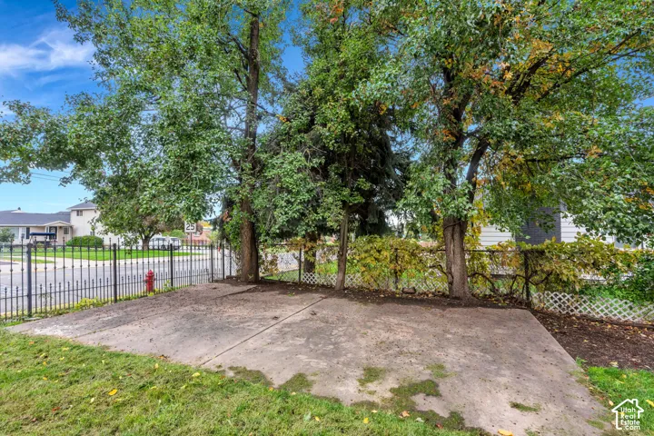 Concrete patio slab bordered by mature trees, metal ornamental fencing, and lattice screen panels
