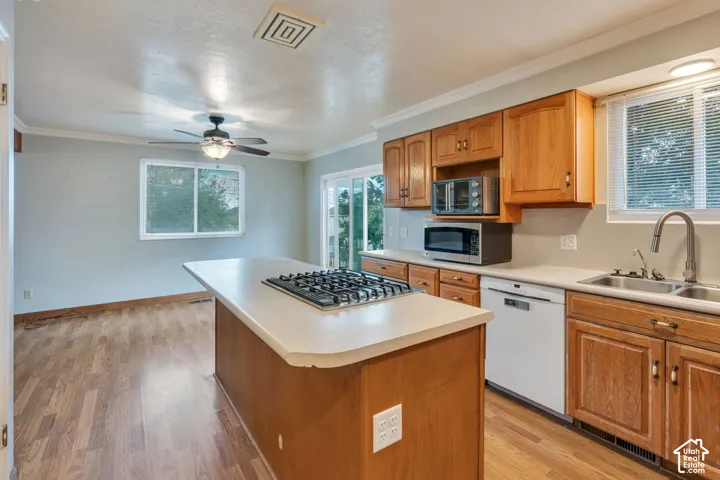 Kitchen featuring wood cabinetry, a central island with a gas cooktop, solid-surface countertops, wood-finish flooring, and a ceiling fan