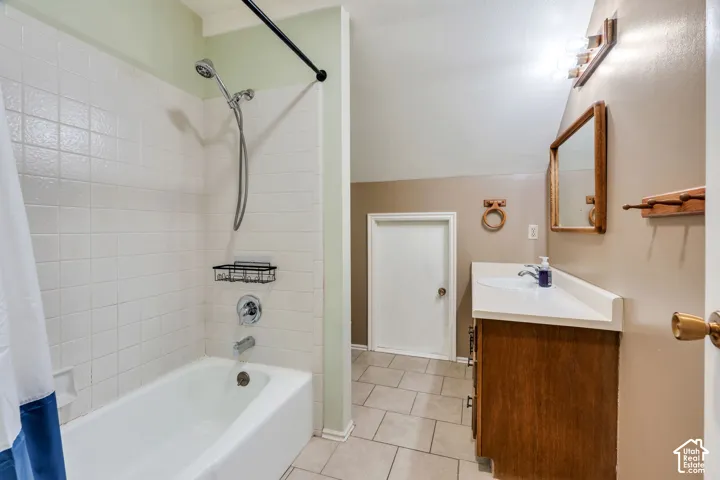 Bathroom featuring a white tub-shower combination with tiled surround, wood-finish vanity cabinet, solid-surface countertop with integrated sink, and ceramic tile flooring