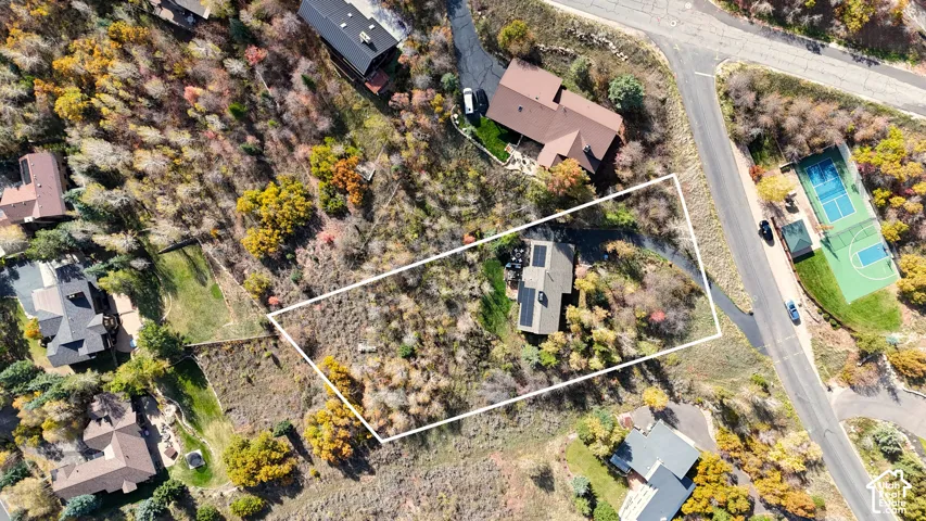 Aerial perspective featuring a detached residential structure, mature native vegetation, asphalt driveway, and solar panel arrays, situated on a secluded lot