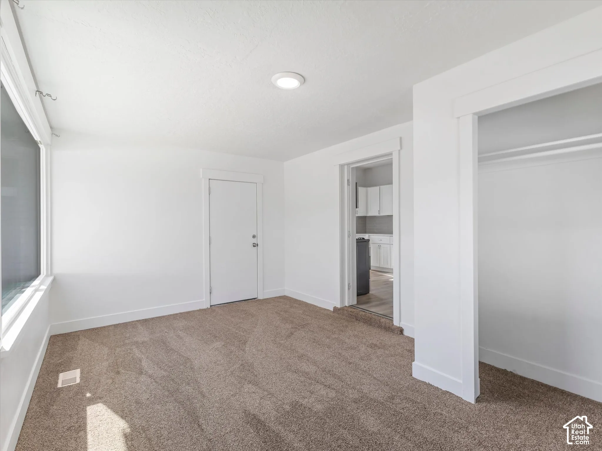 Neutral-toned carpeted flooring, white walls, recessed ceiling lighting, and a built-in closet with overhead shelving