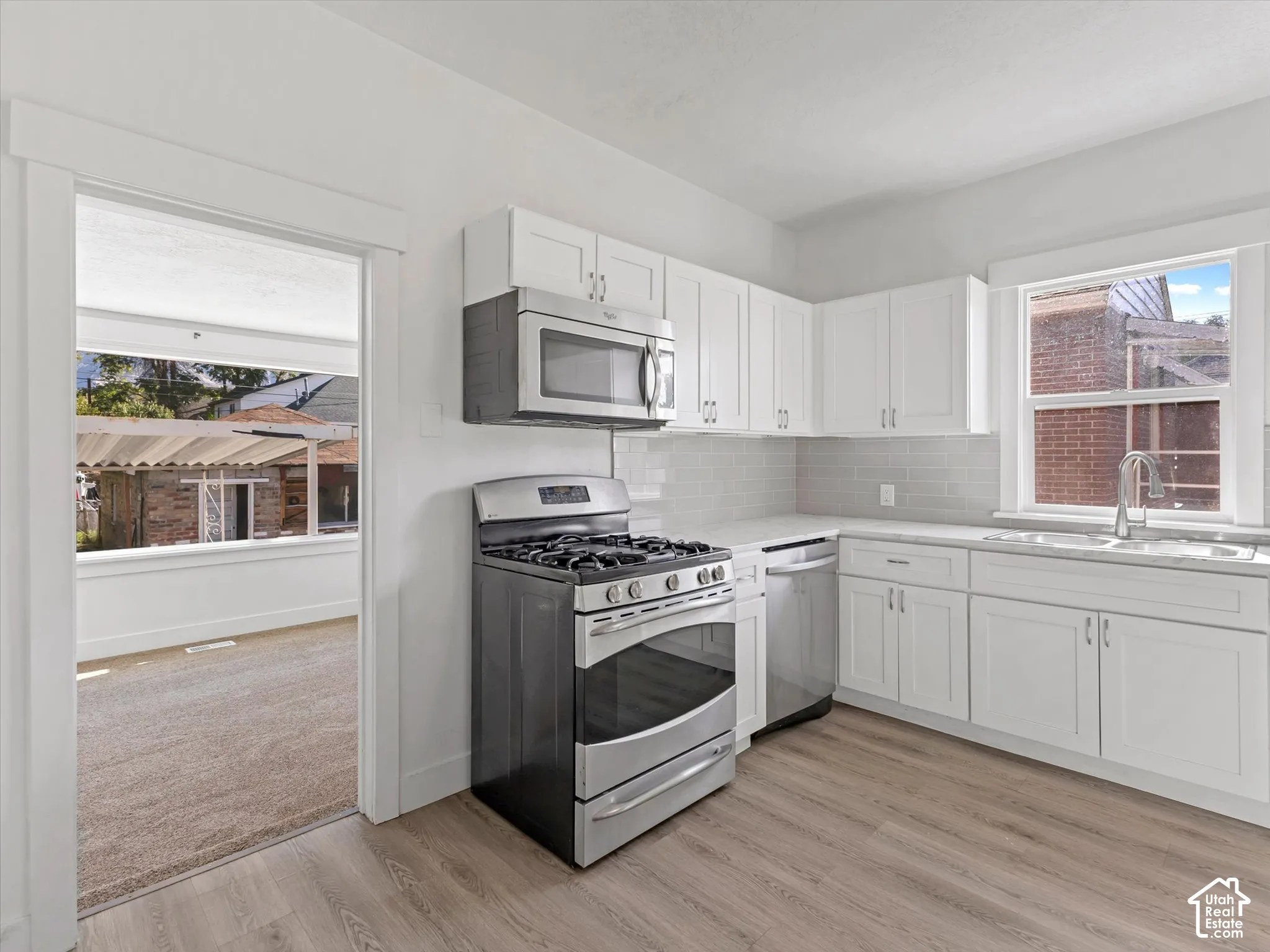 Kitchen featuring white shaker-style cabinetry, stainless steel gas range, over-the-range microwave, subway tile backsplash, and wood-finish flooring