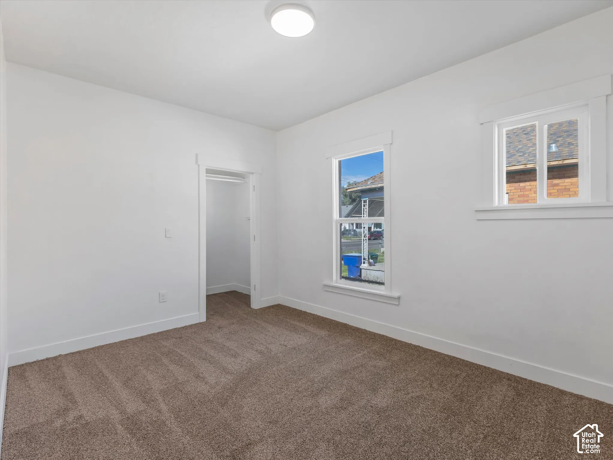 Neutral interior featuring wall-to-wall carpeting, white millwork trim, dual windows, and an interior closet