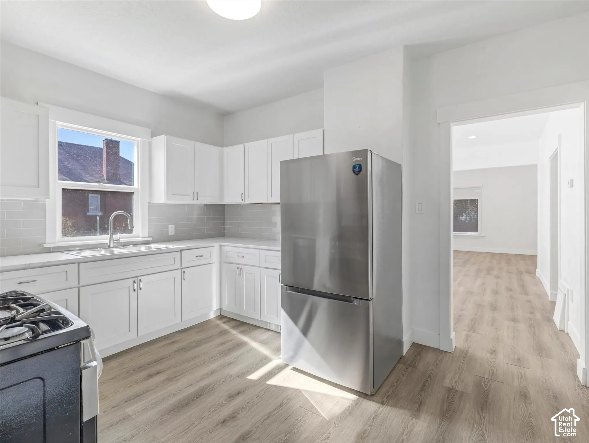 Kitchen featuring white shaker-style cabinetry, stainless steel refrigerator, subway tile backsplash, wood-finish flooring, and a single-basin undermount sink