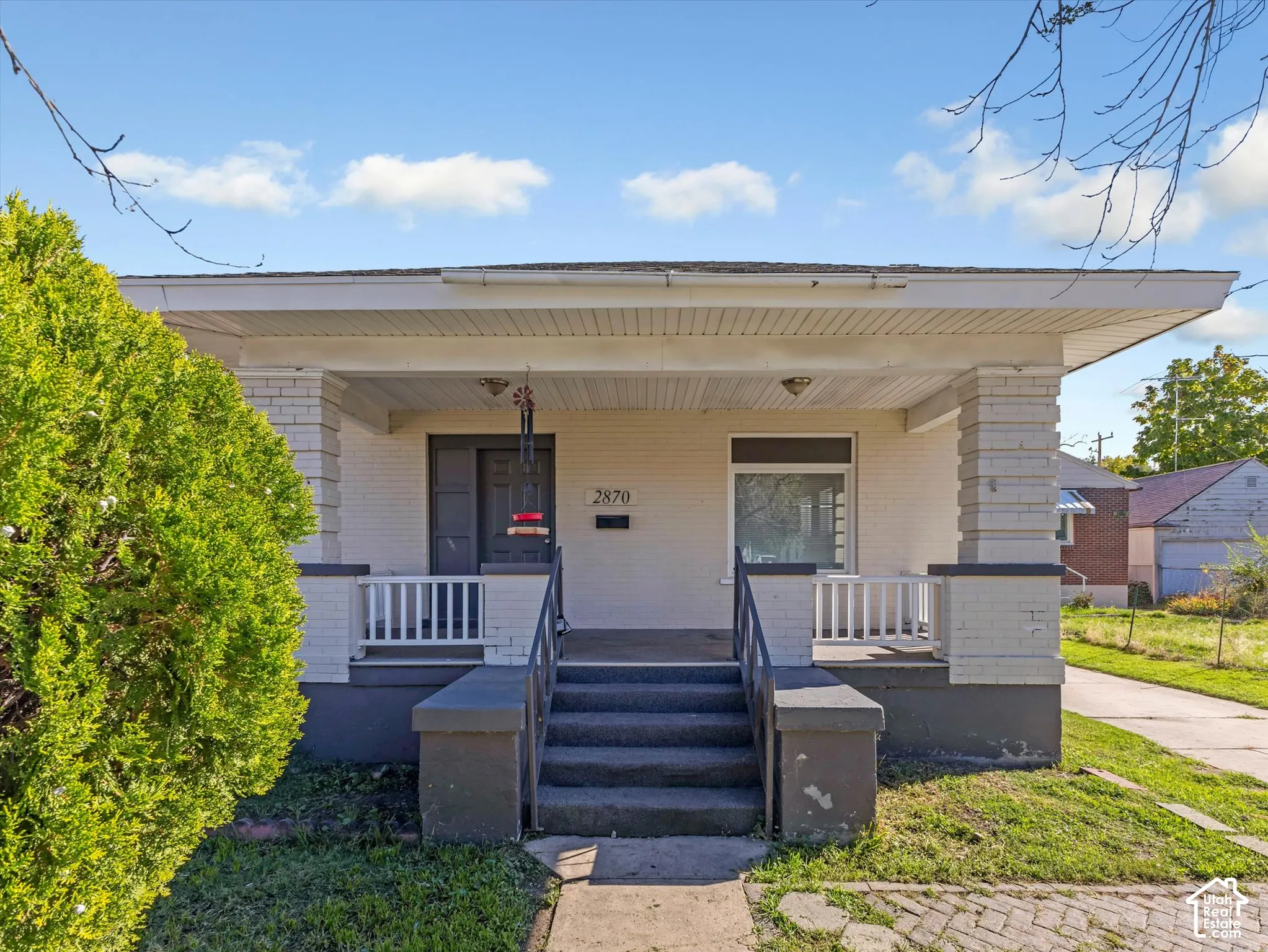 Single-story brick exterior featuring a covered front porch, concrete steps, white railings, and brick-column supports