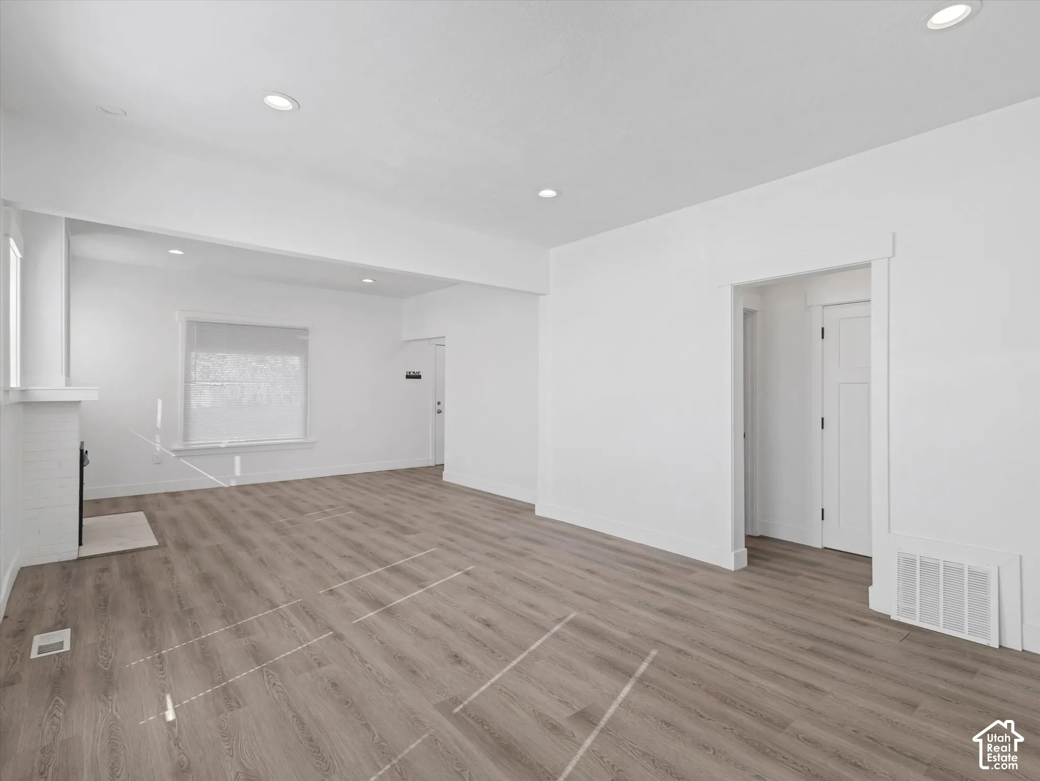 Open-concept interior featuring wood-finish flooring, recessed lighting, and a painted brick fireplace surround