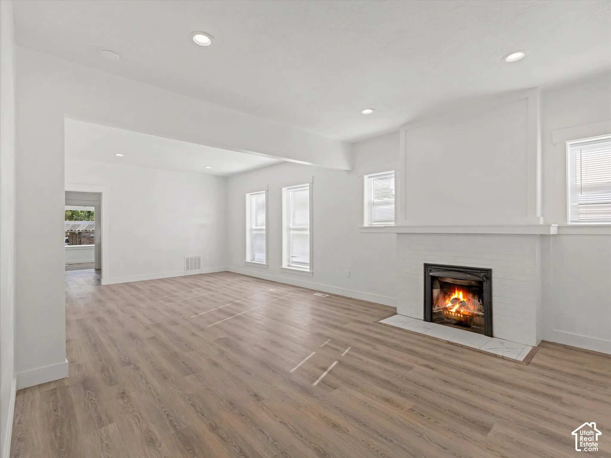 Living area featuring wood-finish flooring, recessed lighting, white-painted brick fireplace, and double-hung windows