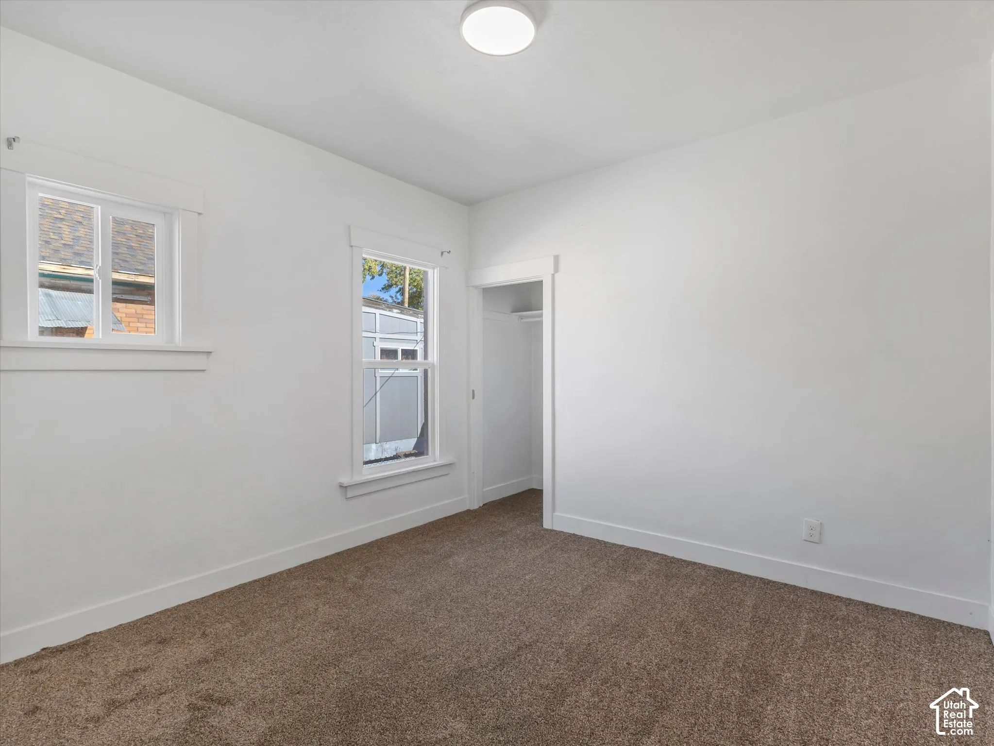 Neutral-toned wall-to-wall carpeting, crisp white walls, dual windows with decorative millwork trim, and a built-in closet with overhead shelving