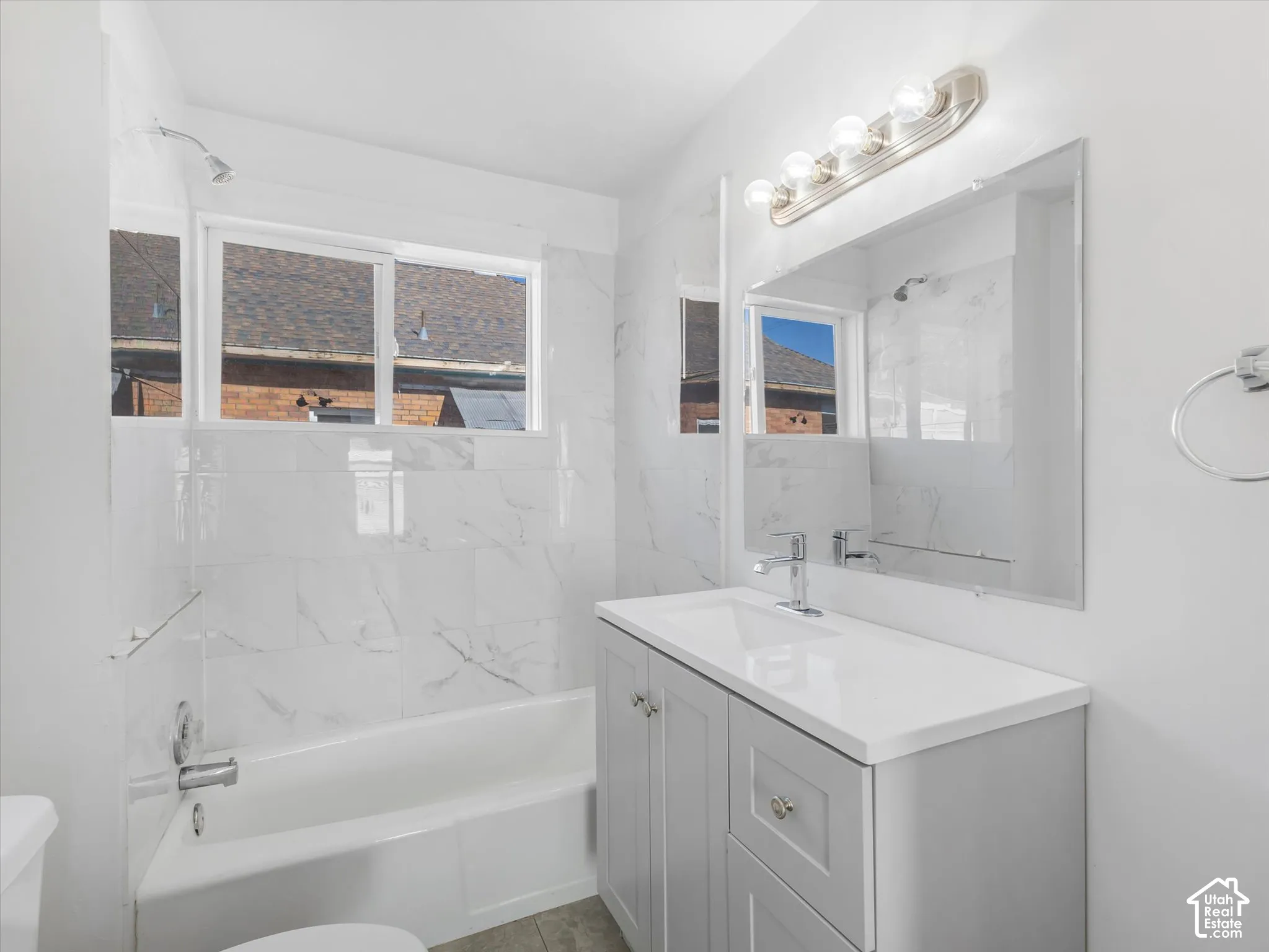 Bathroom featuring a vanity with shaker-style cabinetry and a rectangular undermount sink, large-format tiled tub surround, integrated wall mirror, and five-light vanity fixture