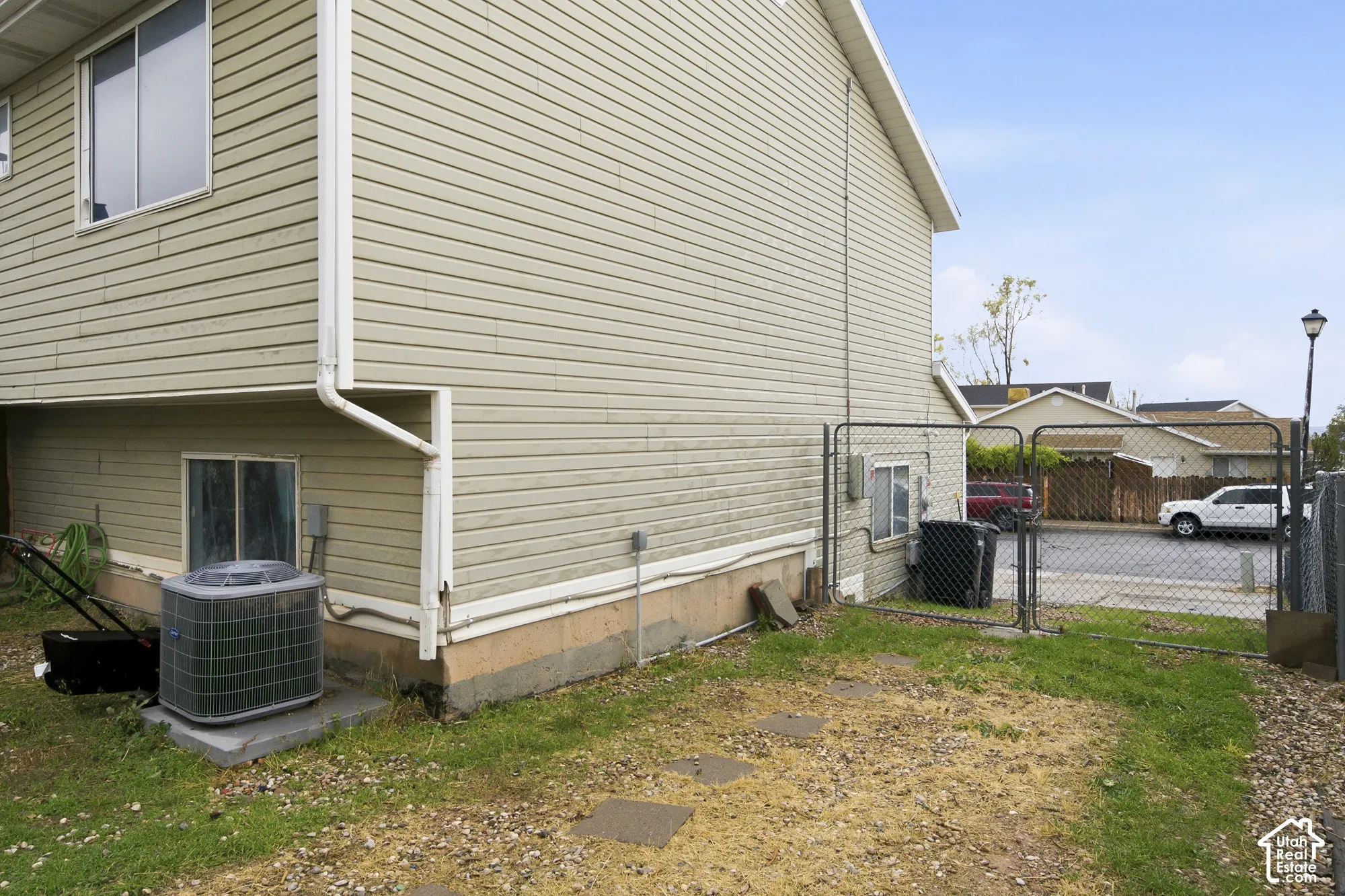 Exterior side yard featuring horizontal vinyl siding, a concrete foundation, a ground-mounted HVAC unit, and metal chain-link fencing