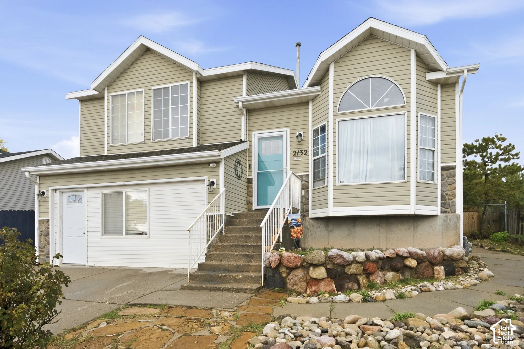 Multi-level exterior featuring horizontal siding, a stone veneer foundation, an attached garage, a bay window with a half-moon accent, and an elevated front entryway with a metal railing