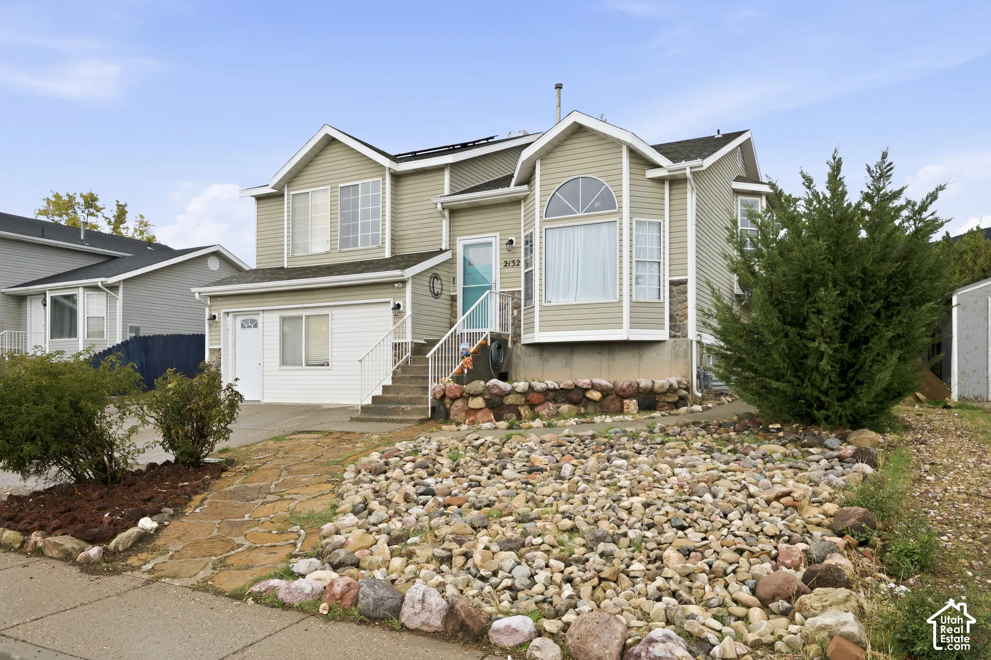 Split-level exterior featuring light-toned horizontal siding, stone foundation accents, a multi-pane arched window, and an attached two-car garage