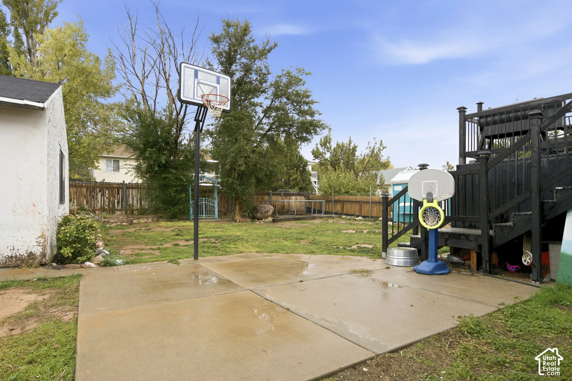 Rear exterior featuring a concrete sports pad with a built-in basketball hoop, a raised deck with metal railings, and wood fencing