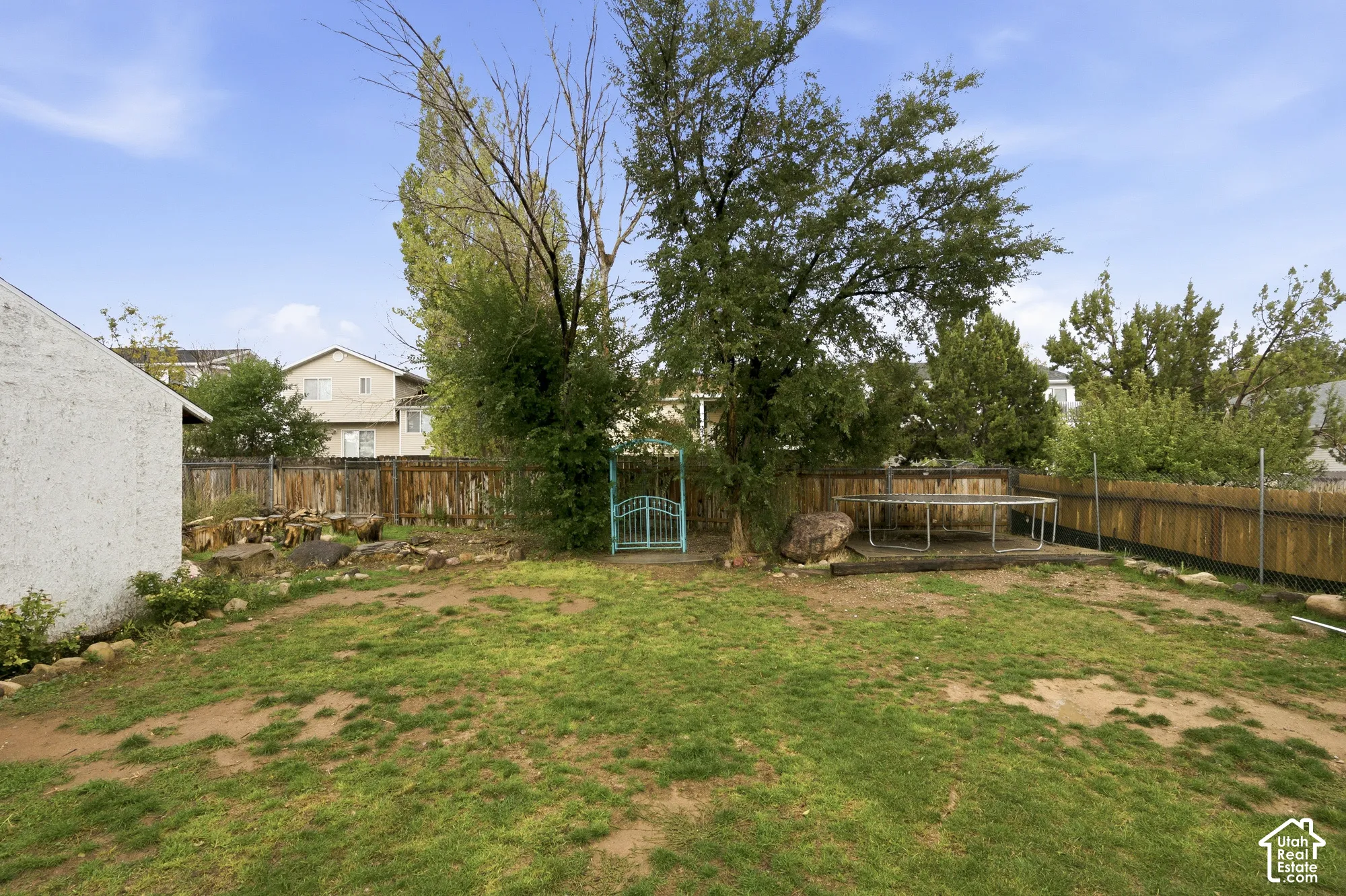 Backyard featuring a wood-panel fence, mature trees, rock landscaping, and a metal arbor