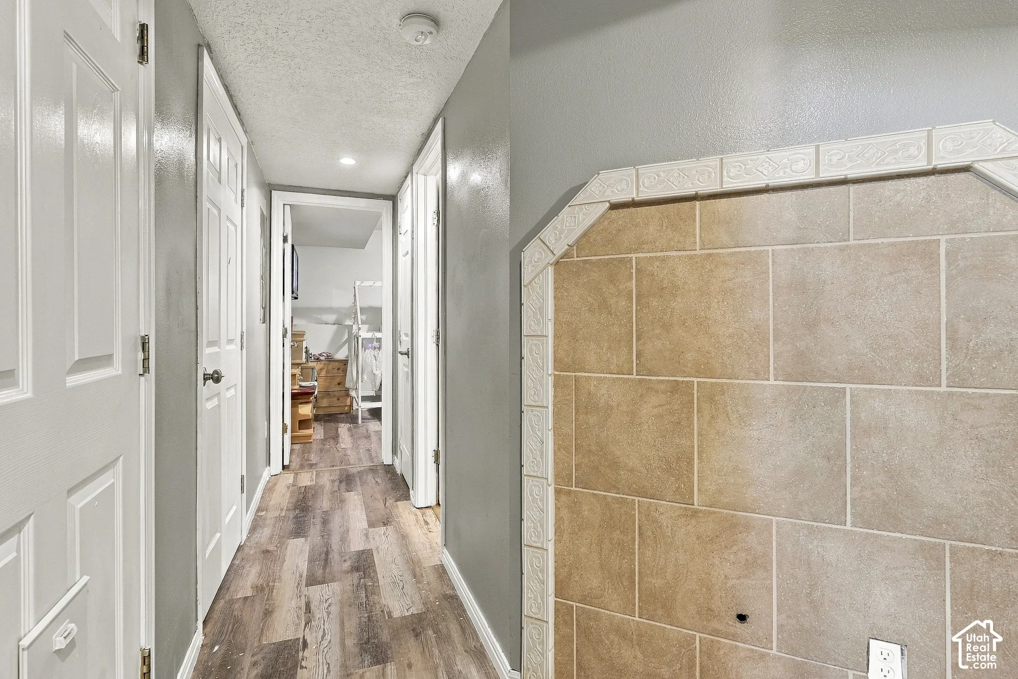 Hallway featuring wood-finish flooring, multi-panel doors, and an accent wall with textured stone-finish tiling and decorative trim