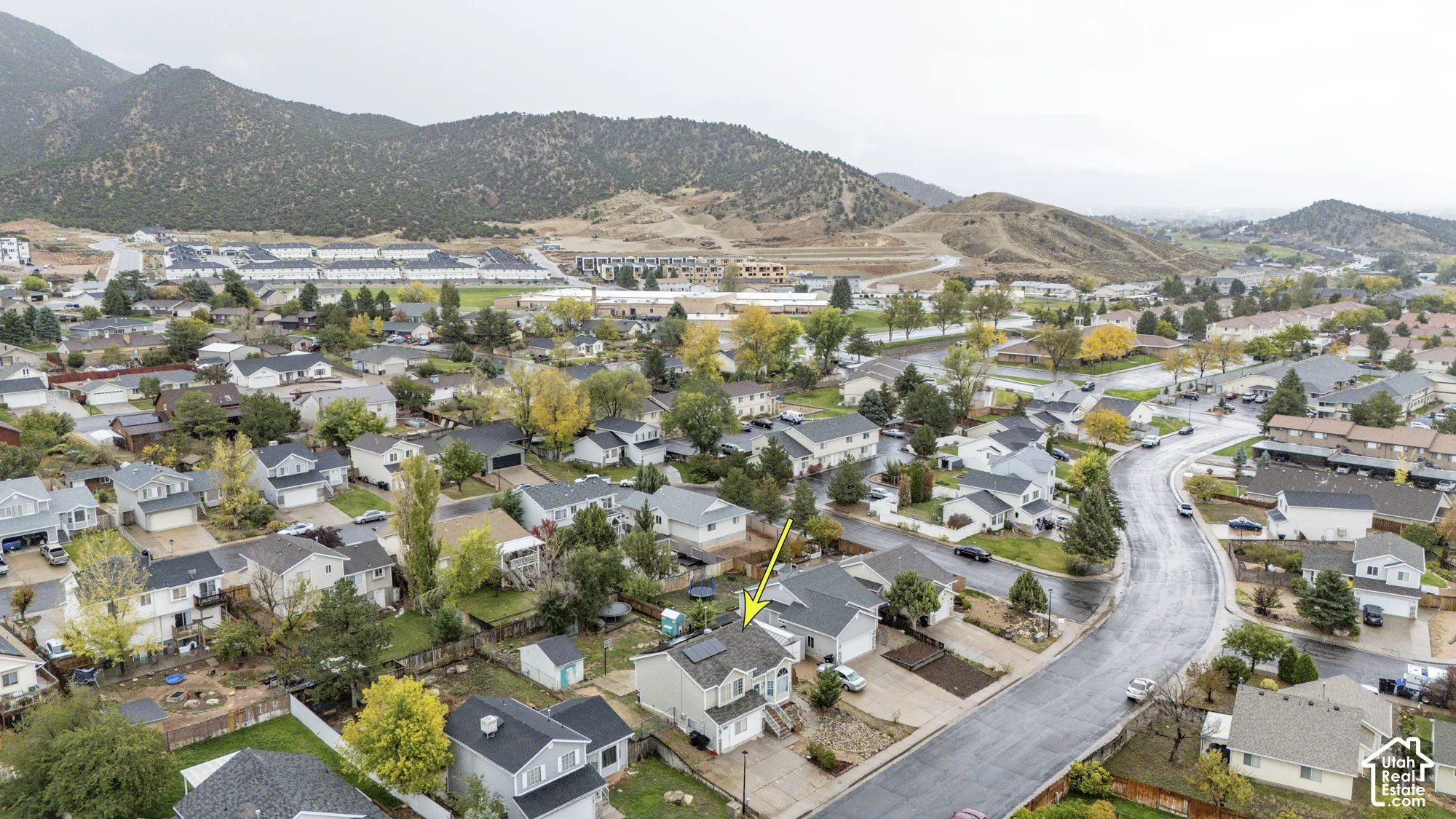 Aerial perspective featuring a two-story residence with a concrete driveway, rooftop solar panels, and mountain terrain backdrop