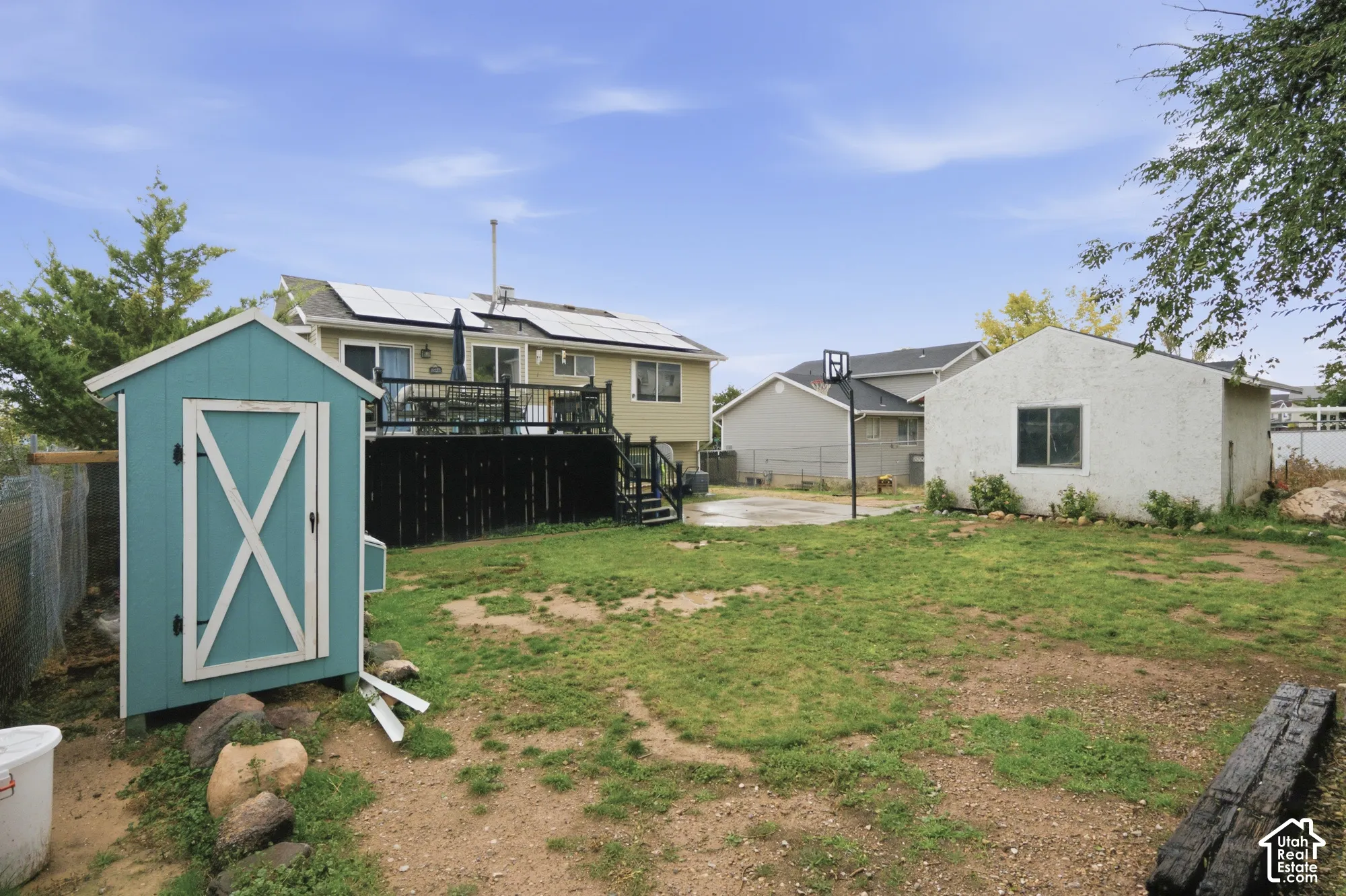 Backyard featuring an elevated deck with black railings, roof-mounted solar panels, a detached structure, and a secondary storage unit