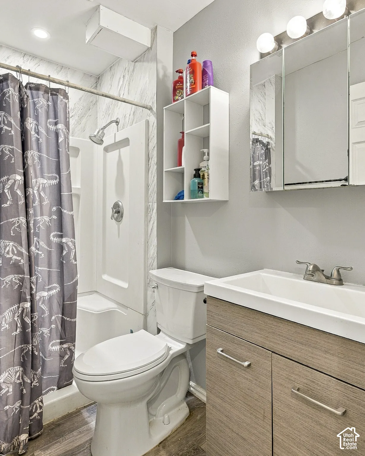 Bathroom featuring a wood-finish vanity with a rectangular sink, triple-bulb light fixture, wall-mounted medicine cabinet, and a shower-tub combination with stone-patterned surround