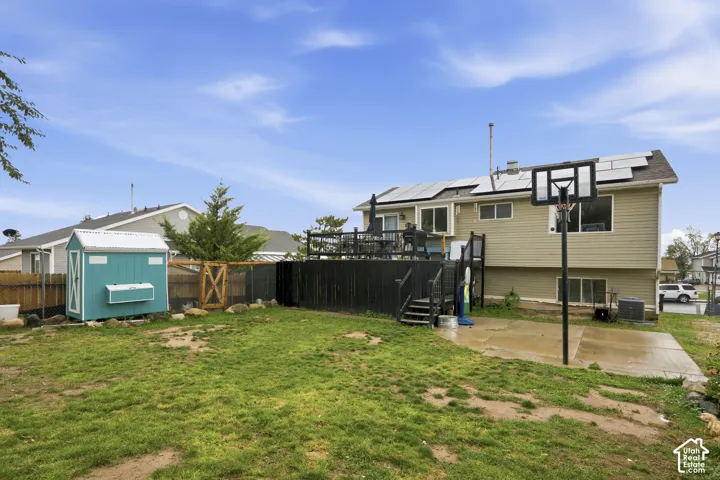 Backyard featuring a raised deck, concrete patio, detached utility structure, and rooftop solar panel array