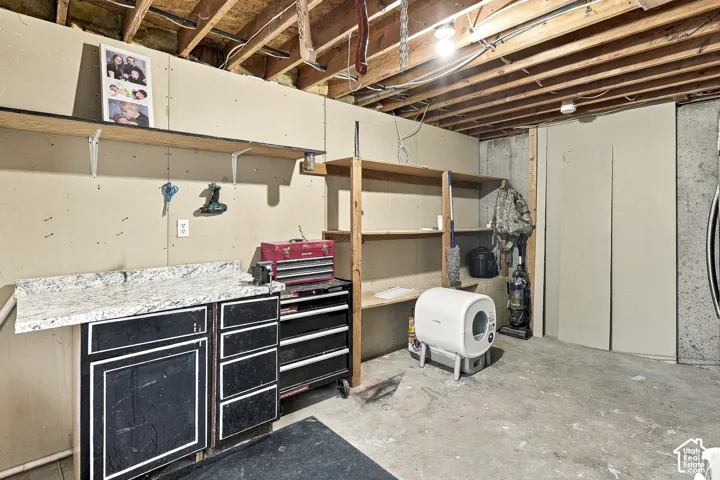 Utility area featuring a built-in cabinet with a stone-finish countertop, exposed ceiling joists, and integrated wooden wall shelving