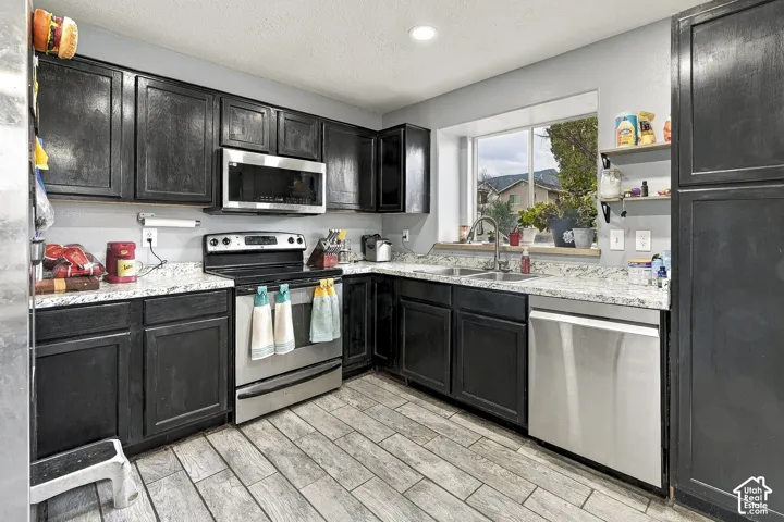 Kitchen featuring dark-finish cabinetry, stone-patterned countertops, stainless steel appliances, and rectangular tile flooring