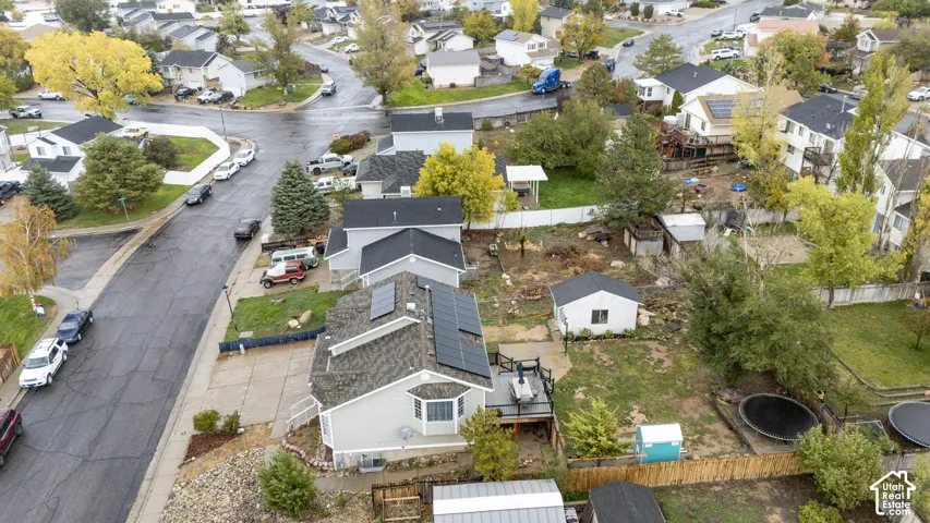 Aerial perspective of a multi-level residence featuring asphalt shingle roofing, integrated solar panel arrays, a raised wood-finish deck, and a detached storage structure