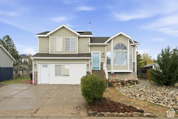 Two-story home with neutral siding, stone veneer accents, multi-pane bay window, attached garage, and stone-paved walkway