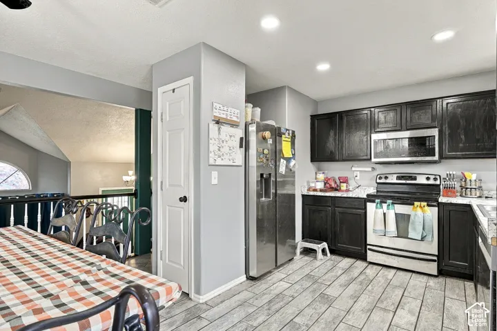 Kitchen featuring dark-finish cabinetry, stone-patterned countertops, stainless steel appliances, recessed ceiling lighting, and wood-finish tile flooring