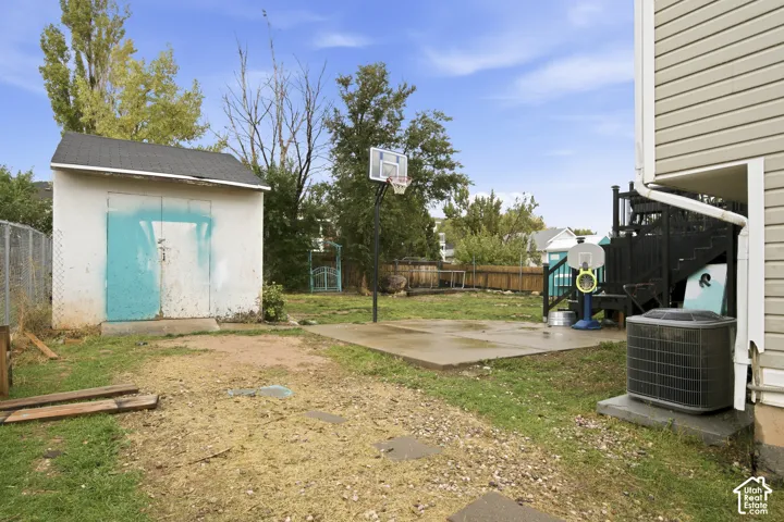 Rear exterior space featuring a concrete patio, detached storage shed, perimeter fencing, and an attached wood deck