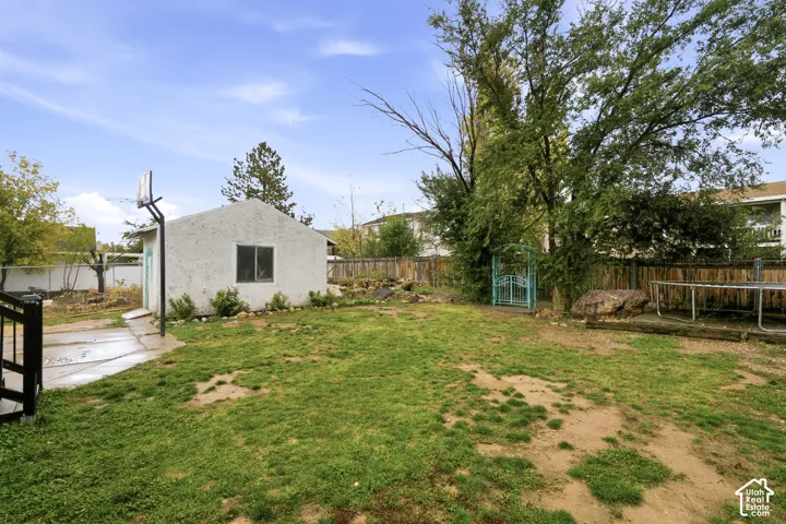 Backyard featuring a detached outbuilding, concrete patio, mature trees, and wood fencing