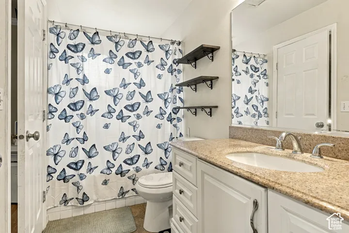 Bathroom featuring a white vanity with stone-composite countertop, undermount sink, polished chrome faucet, three tiered wall-mounted wooden shelves, and a full-width vanity mirror