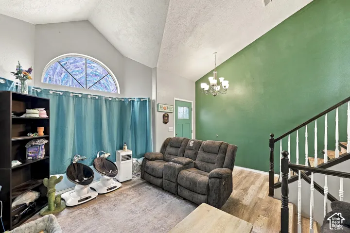Vaulted ceilings, wood-finish flooring, an arched window, a multi-light chandelier, and a staircase featuring a white spindle railing with a black handrail and posts