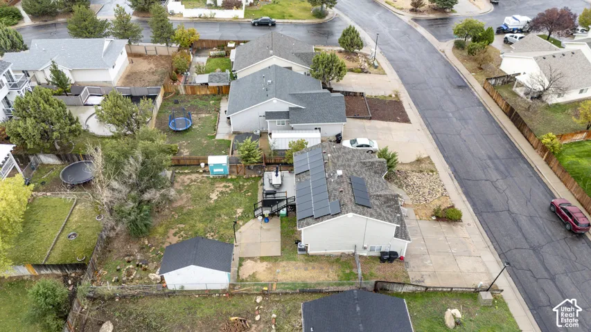 Aerial perspective of a property featuring roof-mounted solar panels, a concrete patio, an attached wood deck, and a detached storage structure situated on a fenced lot